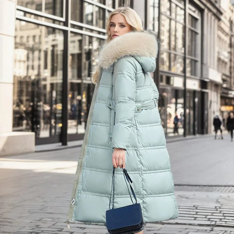 Donna con cappotto lungo imbottito azzurro, cappuccio con pelliccia, borsa blu, cammina in città. Moda invernale, abbigliamento elegante, tendenze 2023.