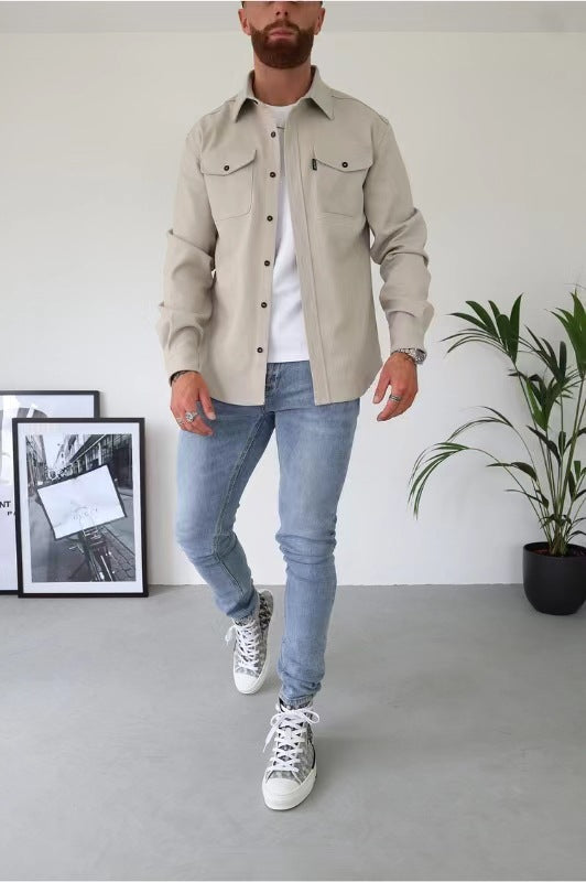 Uomo con camicia beige, jeans chiari e sneakers, in posa casual. Sfondo con piante e quadri. Moda maschile, stile urbano, abbigliamento casual.