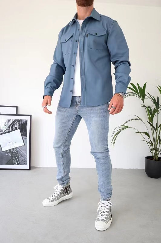 Uomo in camicia blu e jeans chiari, scarpe da ginnastica bianche, in posa moderna. Sfondo minimalista con pianta e quadri. Moda casual maschile.