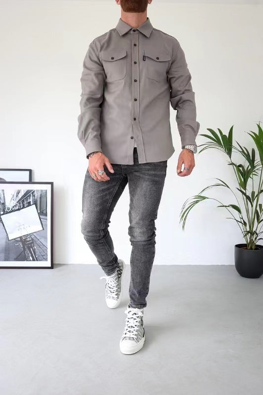 Uomo in camicia grigia e jeans neri, scarpe da ginnastica bianche, in piedi in una stanza moderna con piante e quadri. Moda casual maschile.