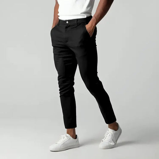 Pantaloni neri eleganti da uomo, abbinati a scarpe da ginnastica bianche e maglietta bianca, su sfondo grigio. Moda maschile casual chic.