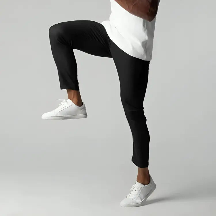 Uomo in pantaloni neri e scarpe bianche, solleva una gamba. Abbigliamento sportivo, moda casual, stile moderno. Sfondo grigio chiaro.