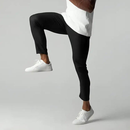 Uomo in pantaloni neri e scarpe bianche, solleva una gamba. Abbigliamento sportivo, moda casual, stile moderno. Sfondo grigio chiaro.