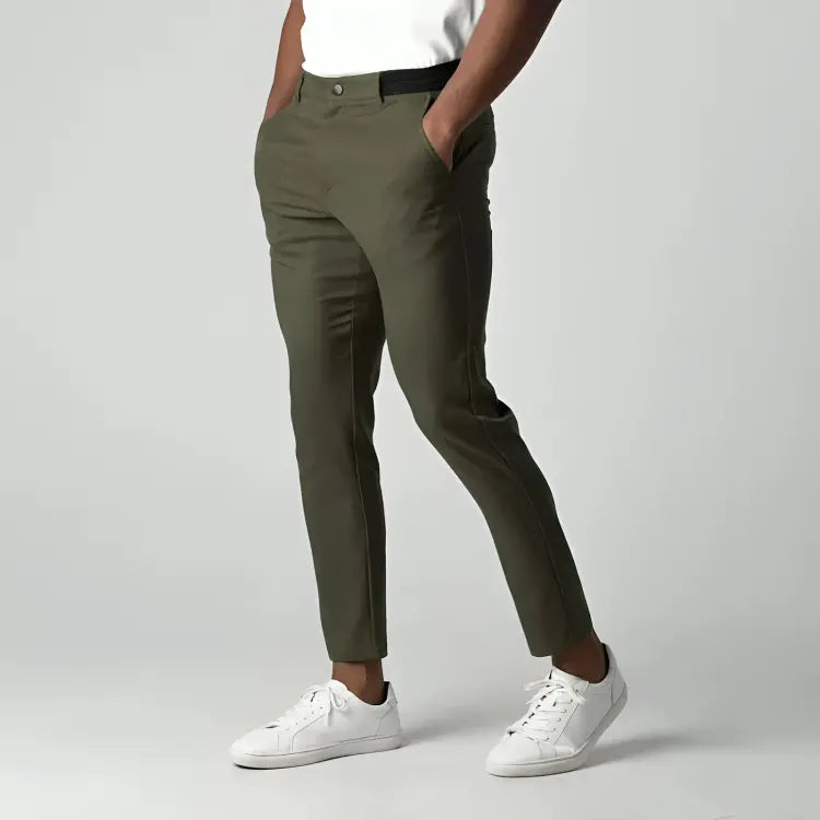 Pantaloni chino verde oliva da uomo, eleganti e moderni, abbinati a scarpe da ginnastica bianche, su sfondo grigio chiaro.