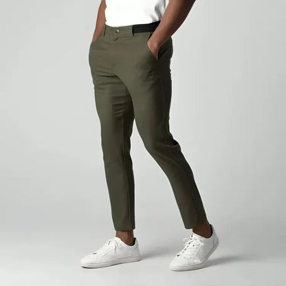 Pantaloni chino verde oliva da uomo, eleganti e moderni, abbinati a scarpe da ginnastica bianche, su sfondo grigio chiaro.