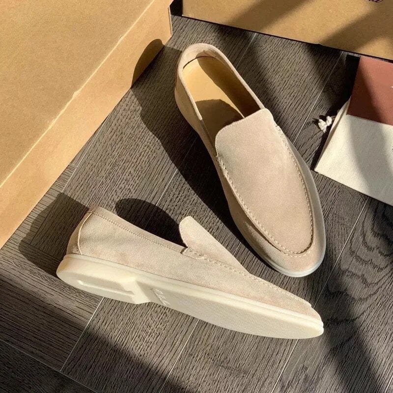 Mocassini beige in pelle scamosciata su pavimento in legno, illuminati dalla luce solare. Scarpe eleganti da uomo, stile casual, moda calzature.