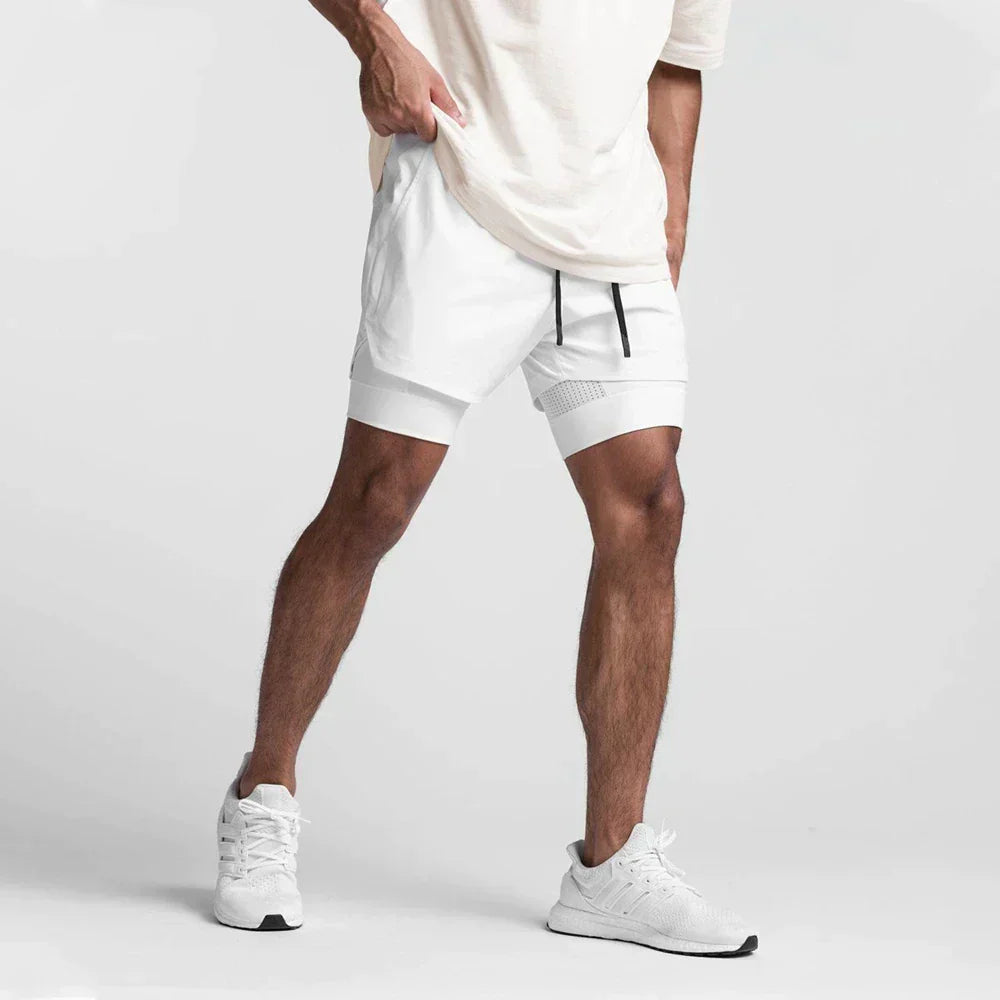 Uomo in pantaloncini sportivi bianchi e scarpe da ginnastica, posa su sfondo grigio. Abbigliamento fitness, moda maschile, stile casual.