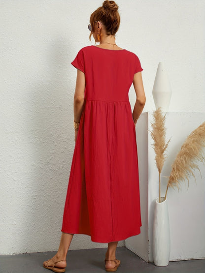 Donna di spalle con abito lungo rosso, sandali beige, accanto a vaso bianco con pampas. Moda estiva, abbigliamento casual elegante.