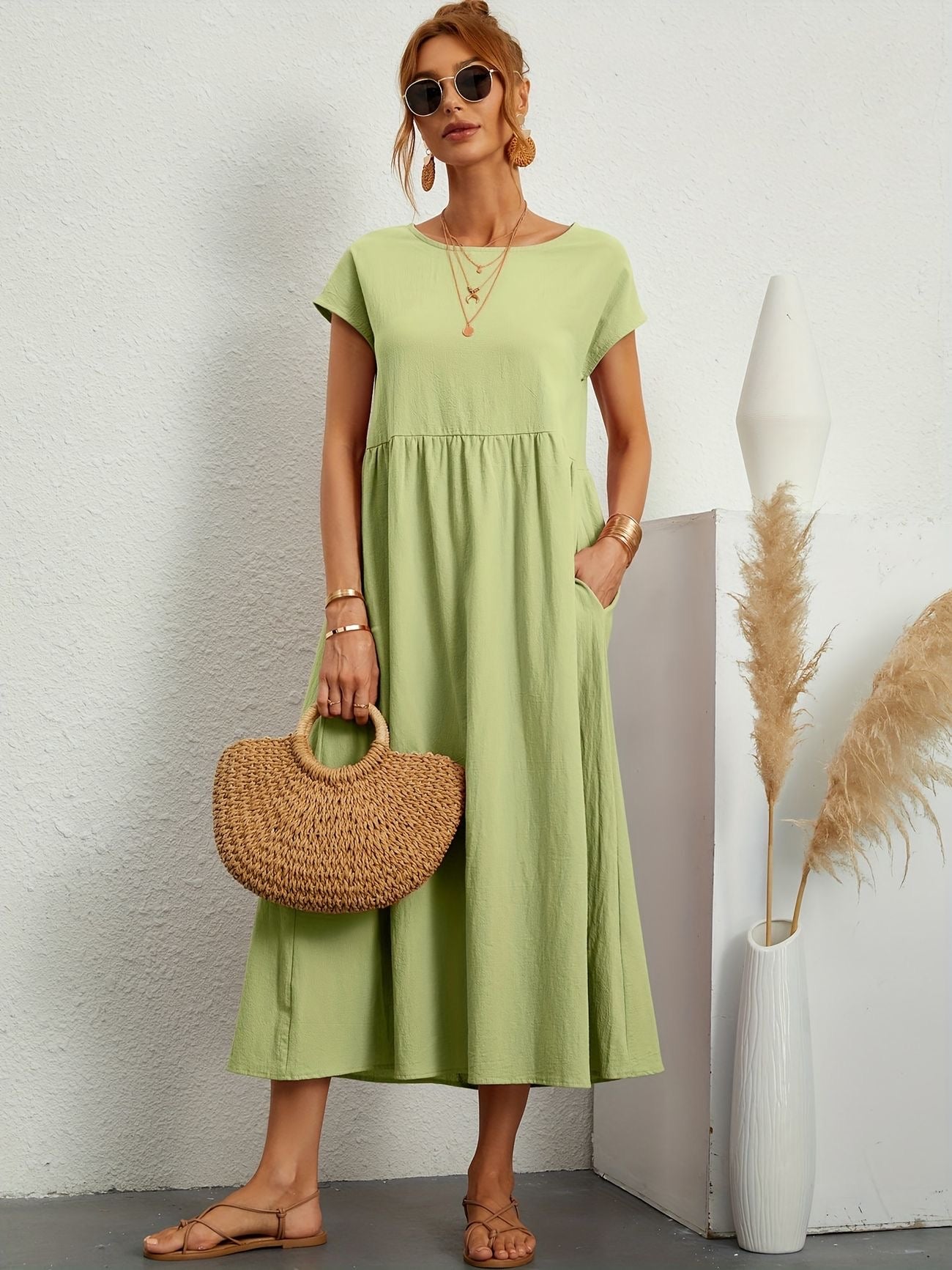 Donna con abito verde chiaro, borsa di paglia, occhiali da sole, sandali beige. Sfondo bianco con decorazioni minimaliste. Moda estiva elegante.
