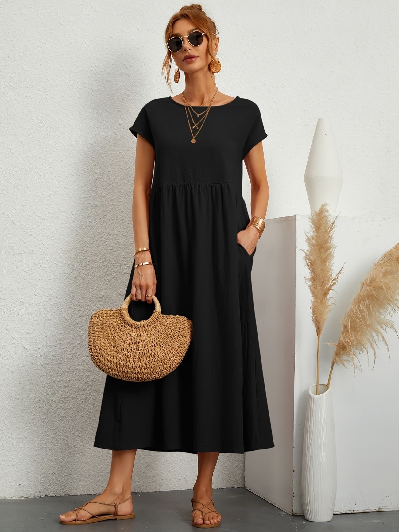 Donna con abito nero lungo, borsa di paglia, occhiali da sole, sandali beige. Sfondo bianco con decorazioni minimaliste. Moda estiva elegante.