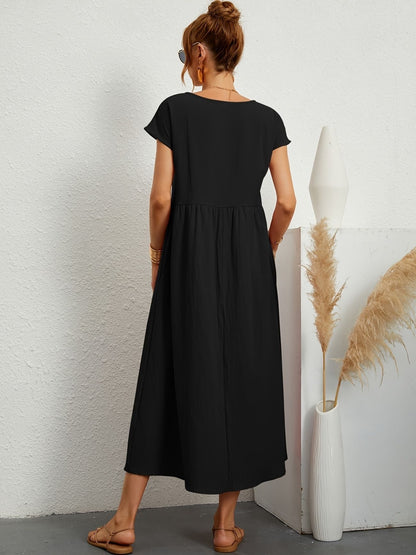 Donna di spalle con abito lungo nero, sandali beige, accanto a vaso bianco con pampas. Moda estiva, abbigliamento casual elegante.