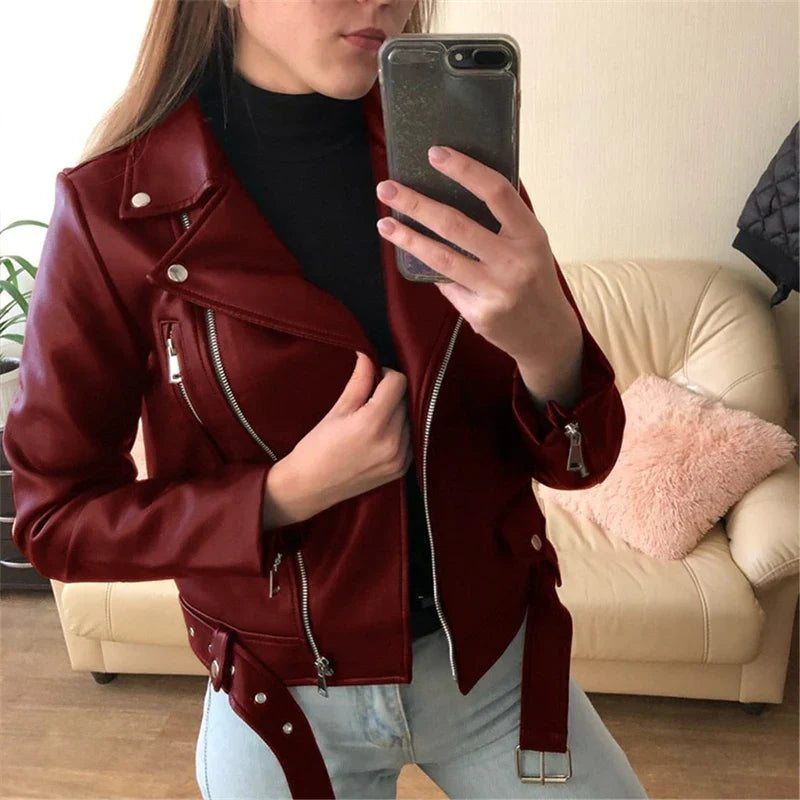 Giacca in pelle rossa da donna, stile motociclista, con zip argentate, indossata sopra un maglione nero. Sfondo con divano beige.