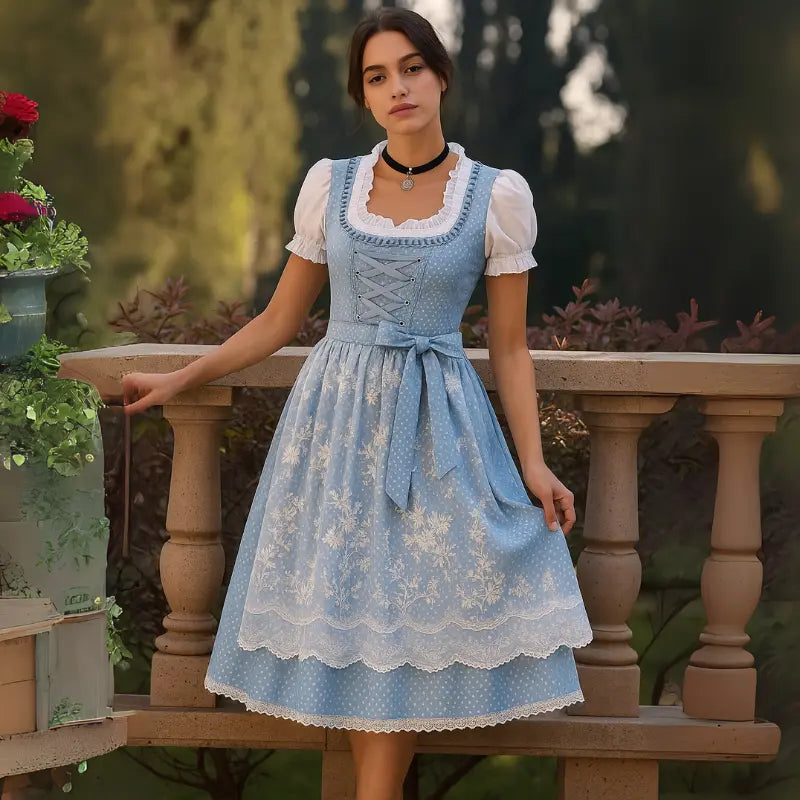 Donna in abito tradizionale bavarese blu con dettagli in pizzo bianco, su balcone con fiori. Moda dirndl, abbigliamento tradizionale tedesco.