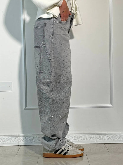 Pantaloni grigi con strass, tasche laterali, indossati con sneakers bianche e nere. Stile casual, moda uomo, abbigliamento trendy.