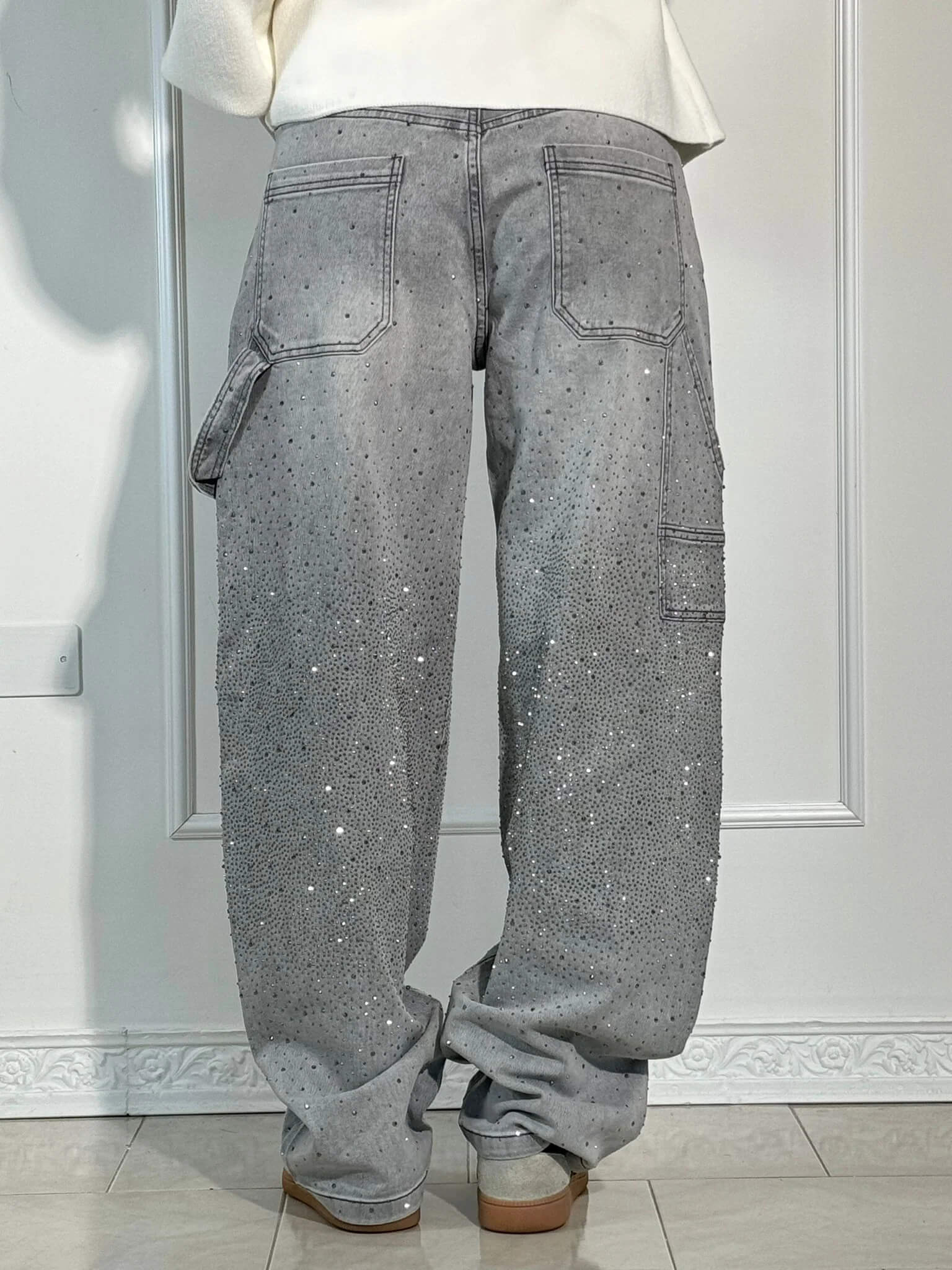 Jeans grigi con strass, tasche posteriori e laterali, indossati da una persona. Design moderno, stile casual, moda autunno-inverno.