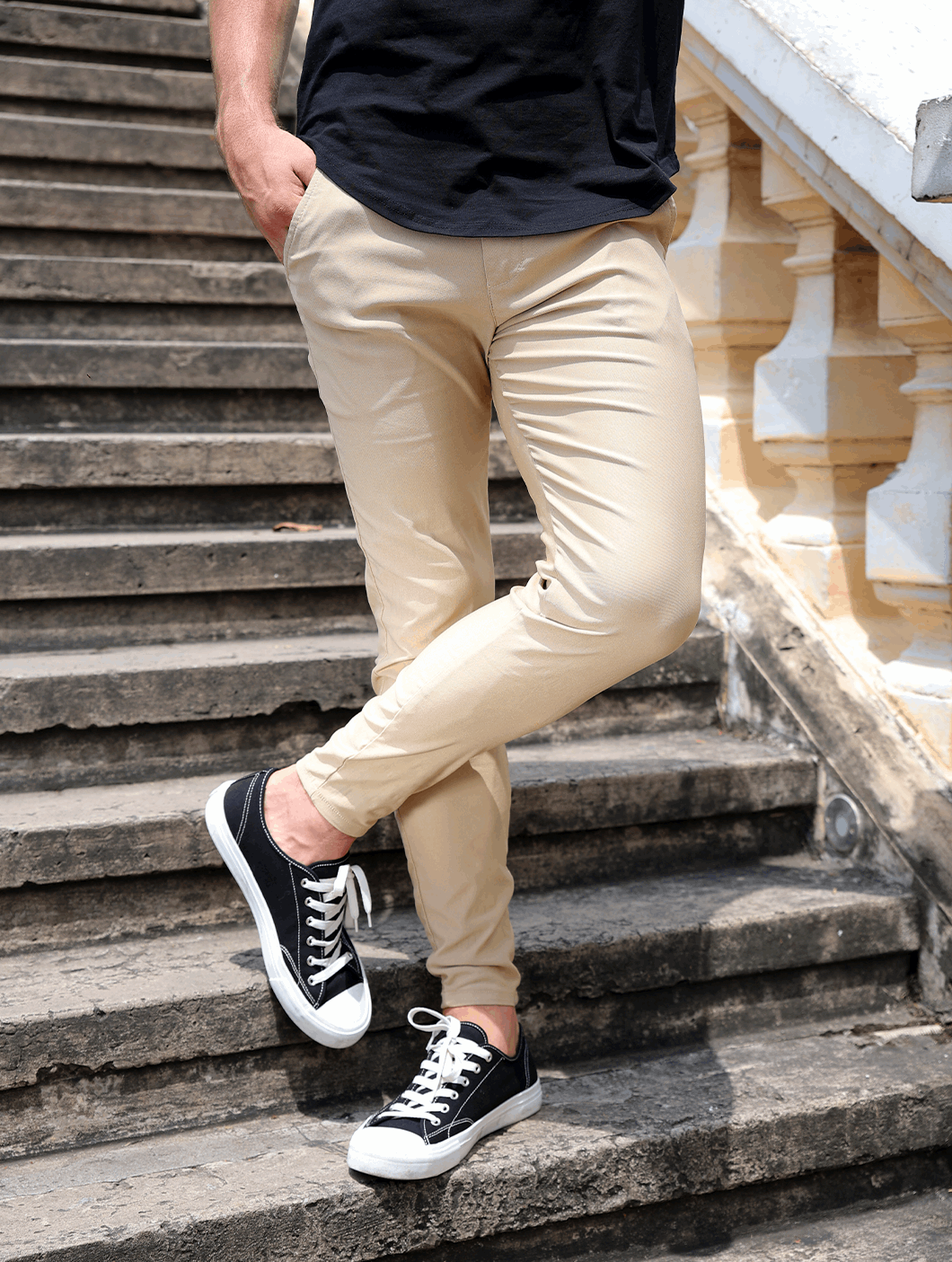 Uomo in pantaloni beige e scarpe da ginnastica nere su scala di pietra. Moda casual maschile, outfit estivo elegante.