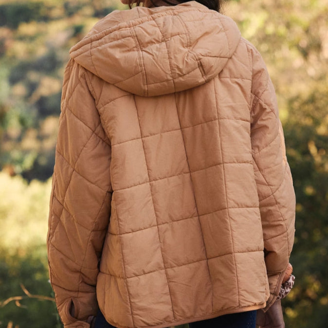 Giacca trapuntata beige con cappuccio, vista posteriore, indossata all'aperto in un ambiente naturale. Moda autunnale, abbigliamento casual.