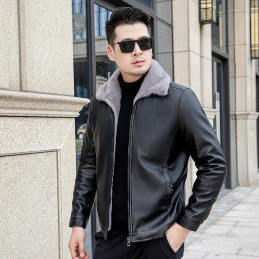 Uomo con giacca di pelle nera e occhiali da sole, posa all'aperto davanti a un edificio moderno. Moda maschile, stile urbano, abbigliamento invernale.