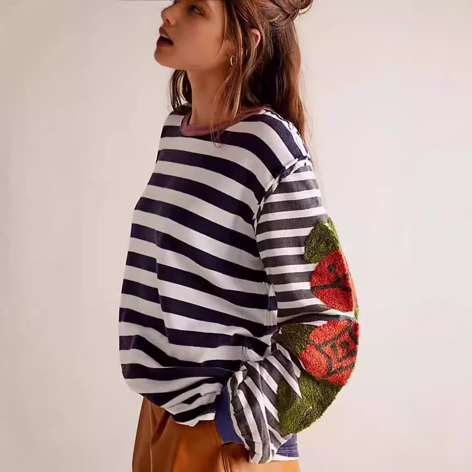 Maglia a righe bianche e blu con toppe floreali sulle maniche, indossata da una donna. Moda casual, stile autunnale, abbigliamento femminile trendy.