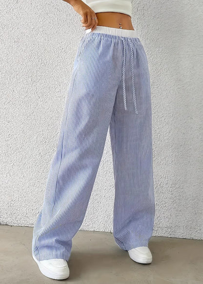 Pantaloni a righe bianche e blu, larghi e a vita alta, indossati con top bianco. Stile casual estivo, moda donna, abbinati a scarpe bianche.