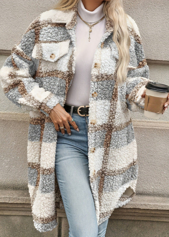 Donna con cappotto a quadri in lana bouclé, camicia bianca a collo alto, jeans chiari, cintura nera, collana dorata, tiene bicchiere di caffè.