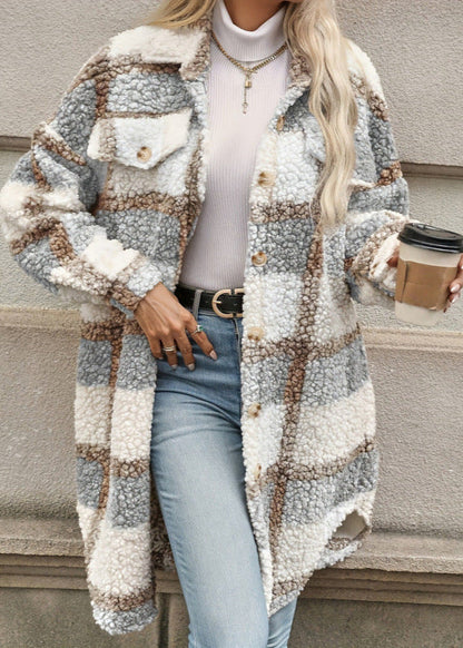 Donna con cappotto a quadri in lana bouclé, camicia bianca a collo alto, jeans chiari, cintura nera, collana dorata, tiene bicchiere di caffè.