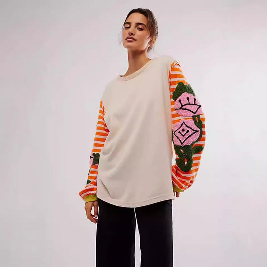 Maglione beige con maniche a righe arancioni e motivi floreali rosa, indossato da una donna. Moda autunnale, abbigliamento casual chic.