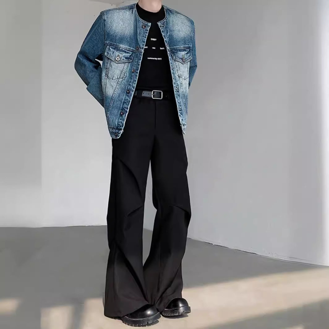 Uomo in giacca di jeans e pantaloni neri larghi, moda casual moderna, scarpe nere, sfondo minimalista. Abbigliamento trendy autunno-inverno.