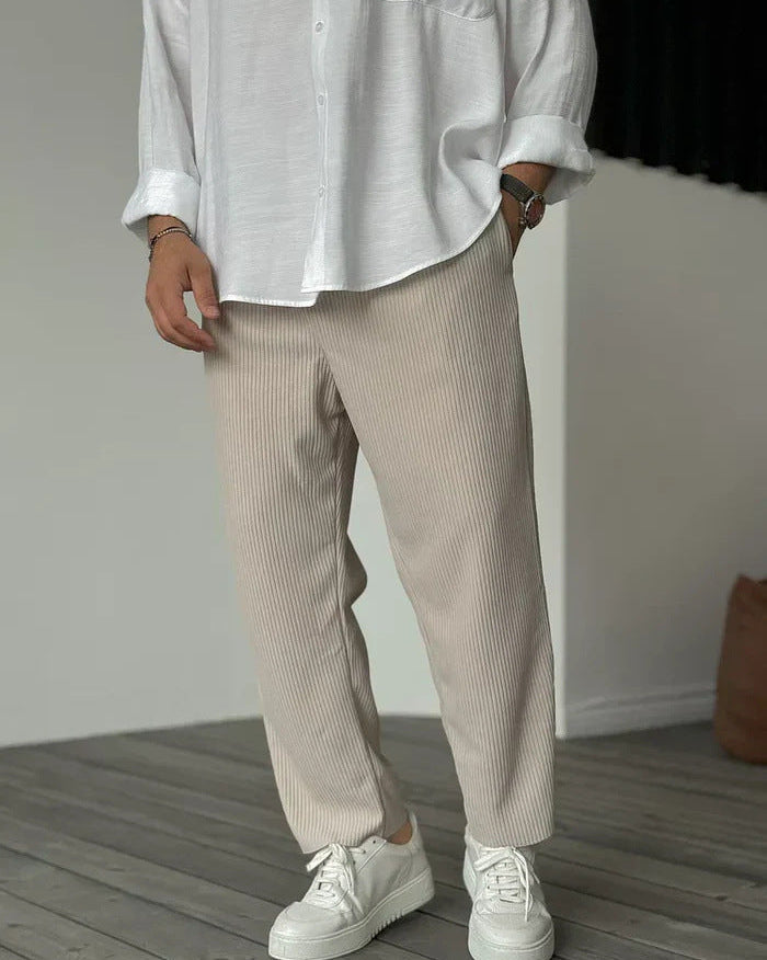 Pantaloni a coste beige, indossati con camicia bianca e sneakers bianche, moda casual uomo, stile minimalista, pavimento in legno.