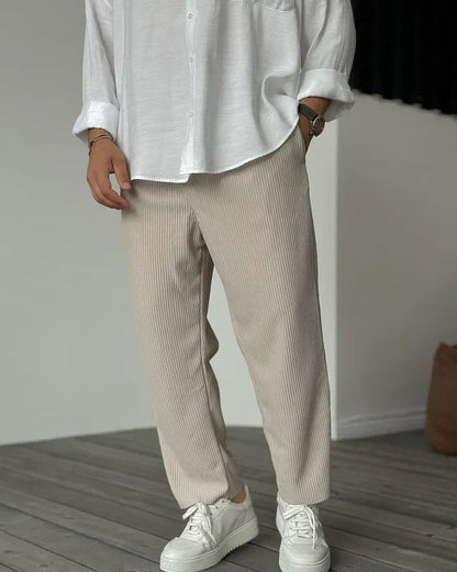 Pantaloni a coste beige, indossati con camicia bianca e sneakers bianche, moda casual uomo, stile minimalista, pavimento in legno.