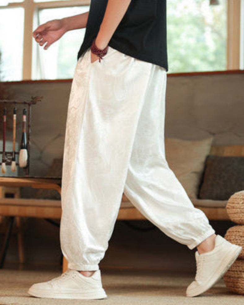 Pantaloni larghi bianchi in seta, stile casual, indossati con scarpe da ginnastica bianche. Look estivo rilassato, moda uomo contemporanea.