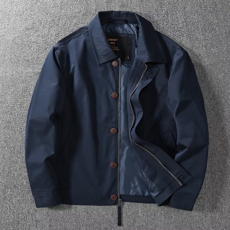 Giacca blu scuro da uomo, stile casual, con bottoni marroni e cerniera, su sfondo grigio. Ideale per moda autunnale e primaverile.