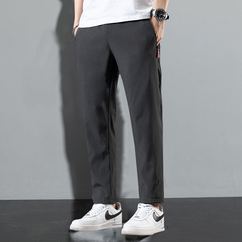Pantaloni neri da uomo, stile casual, abbinati a scarpe da ginnastica bianche Nike, sfondo grigio. Moda maschile, abbigliamento urbano.