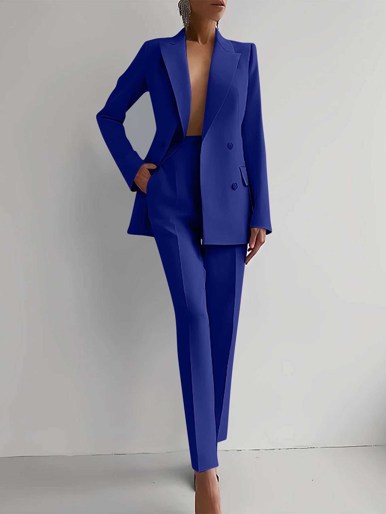 Donna in elegante completo blu, giacca e pantaloni, posa contro sfondo bianco. Moda femminile, abbigliamento formale, stile contemporaneo.