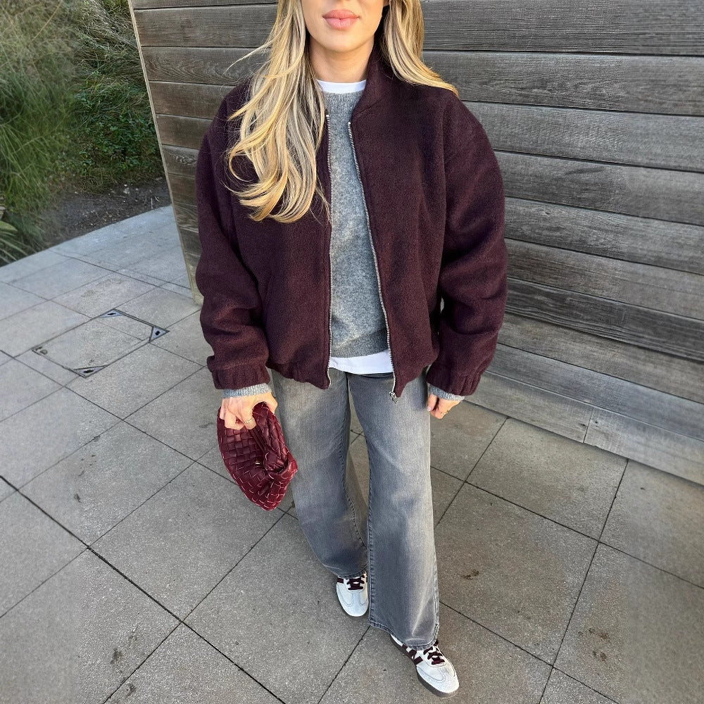 Donna con giacca bordeaux, maglione grigio, jeans larghi e sneakers bianche. Borsa trapuntata rossa. Moda casual autunnale.