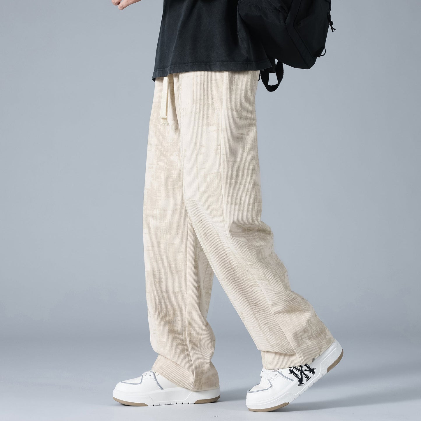 Pantaloni larghi beige in lino, stile casual, indossati con scarpe da ginnastica bianche e zaino nero. Moda uomo, abbigliamento estivo trendy.