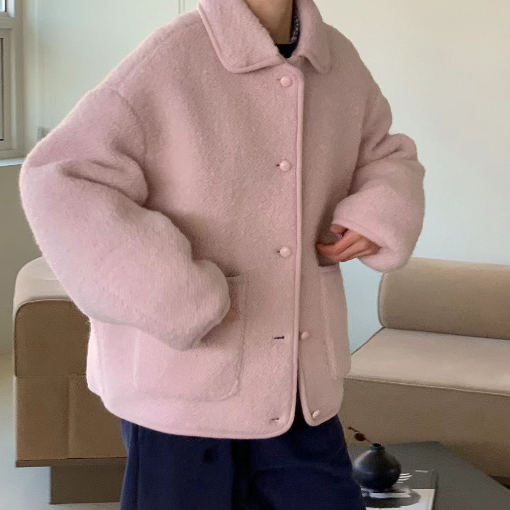 Giacca oversize rosa in lana bouclé, con bottoni e tasche frontali, indossata in un ambiente interno moderno. Moda autunno inverno, stile casual.