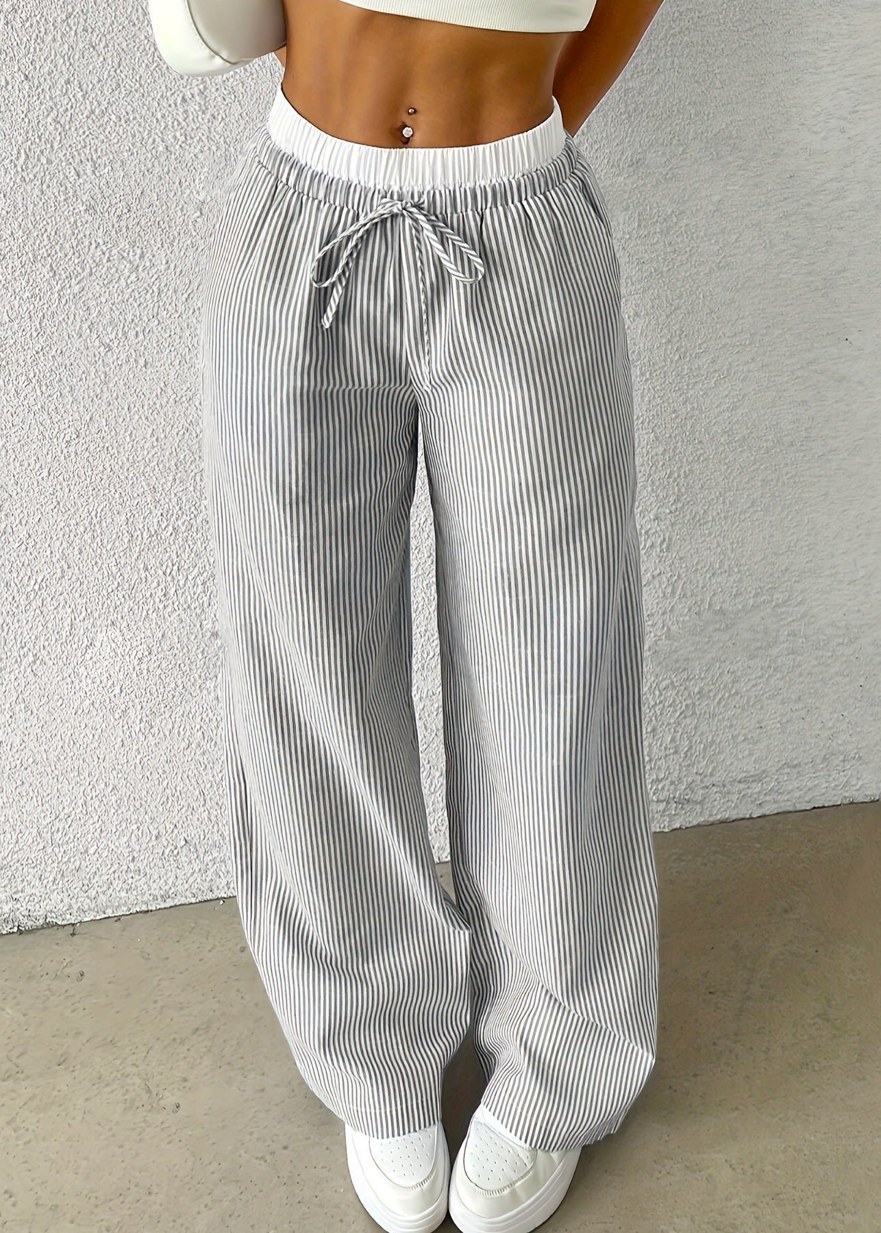 Pantaloni a righe bianche e grigie, larghi e a vita alta, con coulisse, indossati con top corto bianco. Stile casual e moderno.