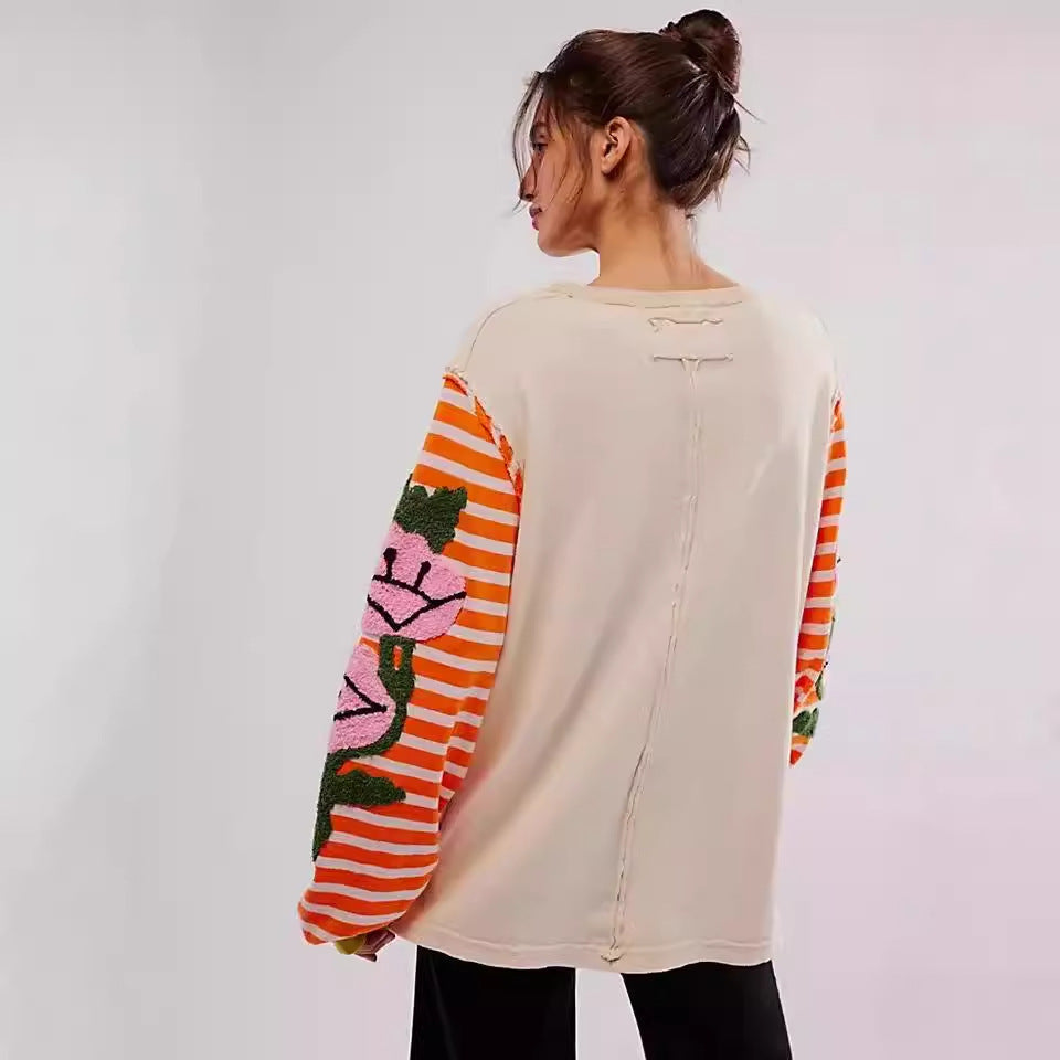 Donna di spalle con maglia oversize beige, maniche a righe arancioni e rosa con motivi floreali. Moda casual, abbigliamento autunnale trendy.