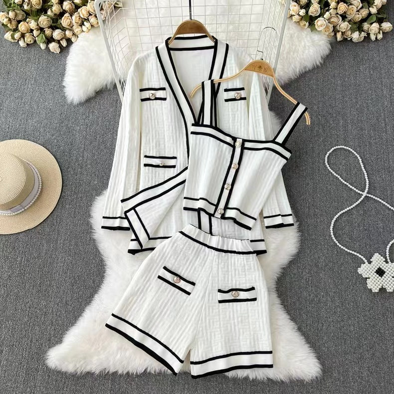 Completo estivo donna bianco a righe nere, composto da giacca, top e shorts. Elegante e casual, ideale per moda estiva. Sfondo con cappello e fiori.