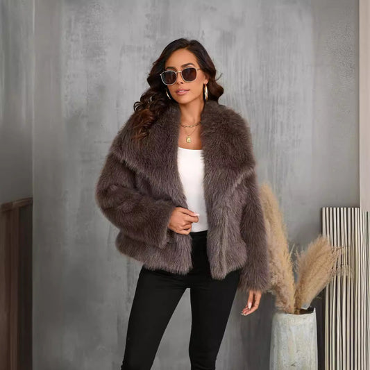 Donna con occhiali da sole indossa giacca di pelliccia marrone, top bianco e pantaloni neri, posa in interni moderni. Moda autunno inverno elegante.