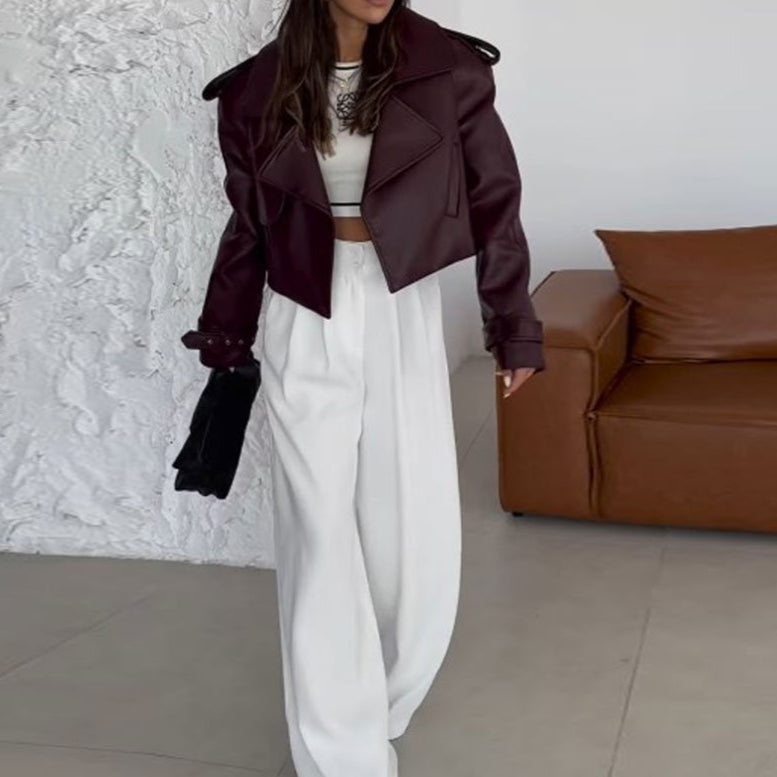 Giacca in pelle bordeaux su donna con pantaloni bianchi larghi, top bianco, borsa nera. Moda autunnale elegante, stile casual chic.