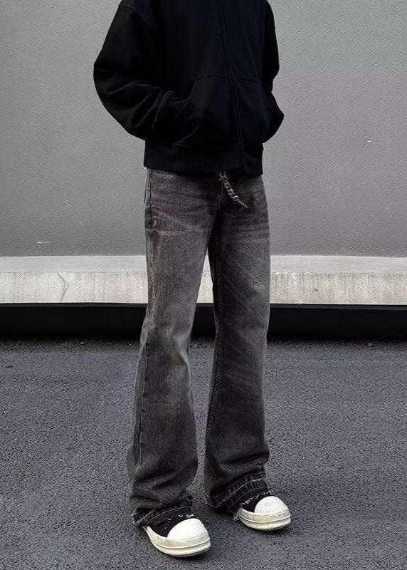 Uomo in felpa nera e jeans grigi larghi, scarpe da ginnastica bianche e nere, posa su sfondo grigio. Moda casual streetwear urbana.