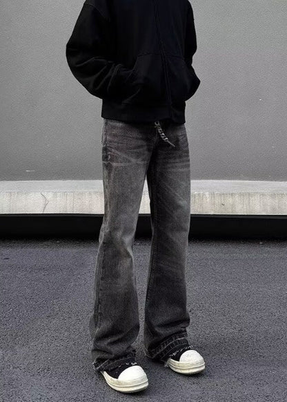 Uomo in felpa nera e jeans grigi larghi, scarpe da ginnastica bianche e nere, posa su sfondo grigio. Moda casual streetwear urbana.