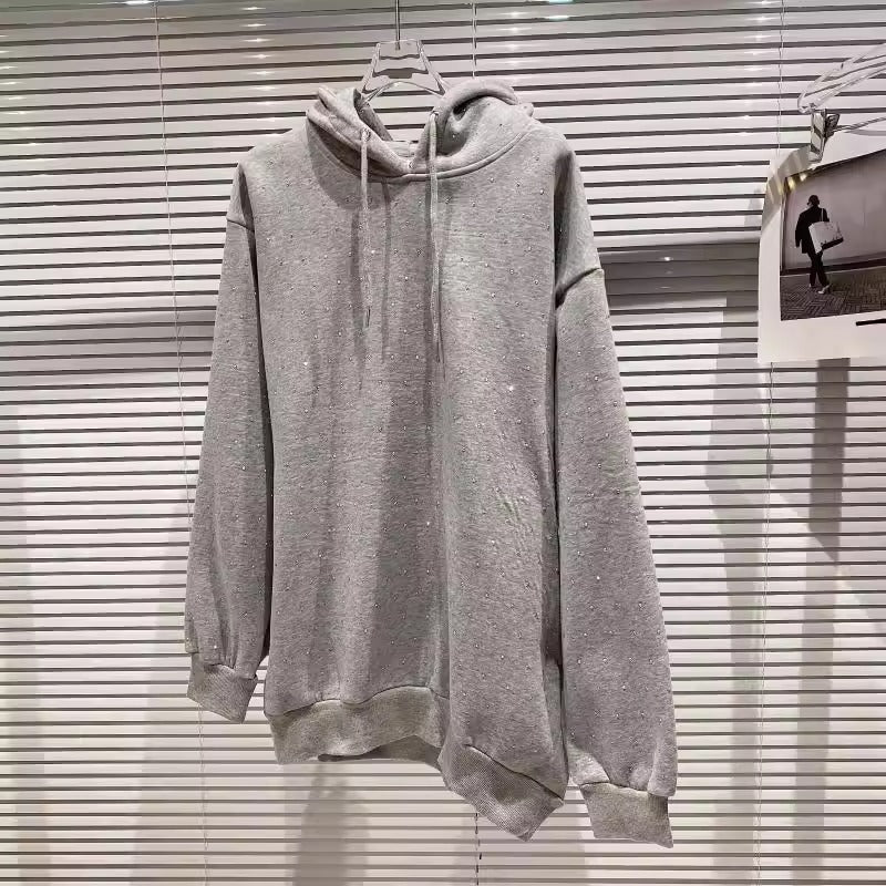Felpa con cappuccio grigia appesa su gruccia, sfondo con veneziane bianche. Abbigliamento casual, moda streetwear, tendenza autunno inverno.