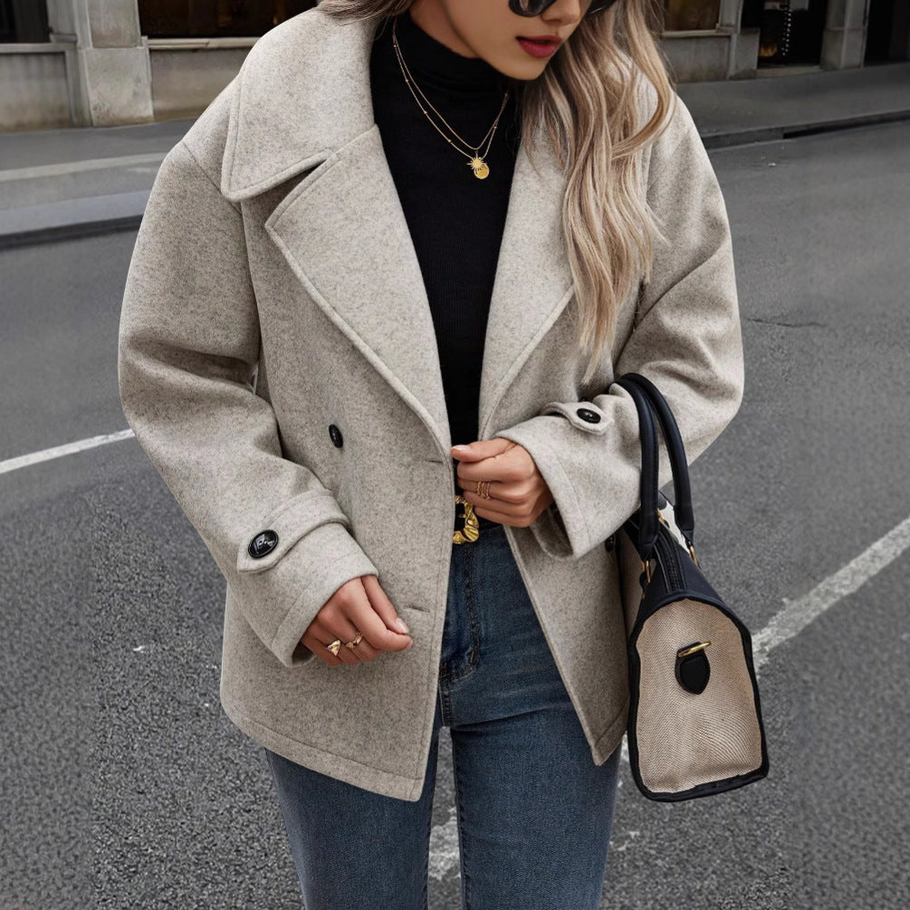 Donna con cappotto beige elegante, maglia nera e jeans, tiene una borsa alla moda. Stile autunnale urbano, moda femminile contemporanea.
