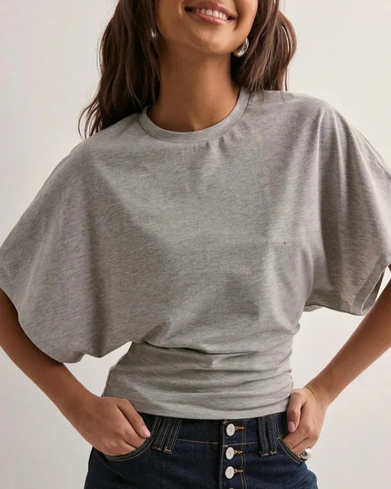 Donna sorridente con maglietta grigia oversize e jeans blu. Moda casual, abbigliamento comodo, stile quotidiano.