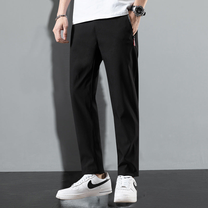 Pantaloni neri eleganti da uomo, abbinati a scarpe sportive bianche Nike, su sfondo grigio. Moda maschile casual e moderna.