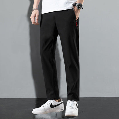 Pantaloni neri eleganti da uomo, abbinati a scarpe sportive bianche Nike, su sfondo grigio. Moda maschile casual e moderna.