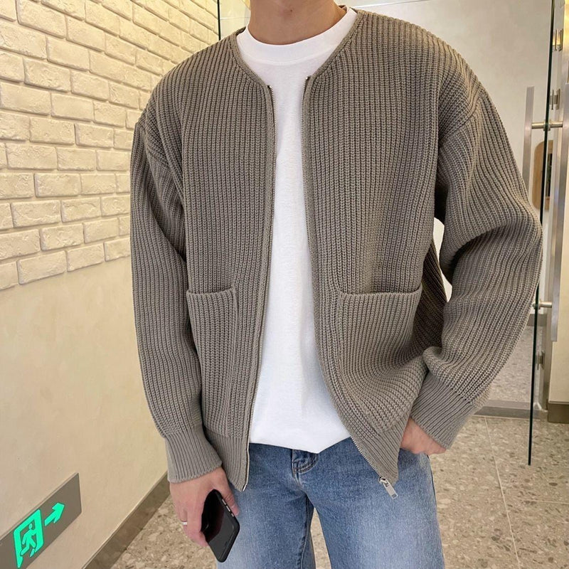 Uomo con cardigan grigio a maglia, tasche frontali, indossa jeans blu e maglietta bianca. Moda casual autunnale, stile urbano moderno.